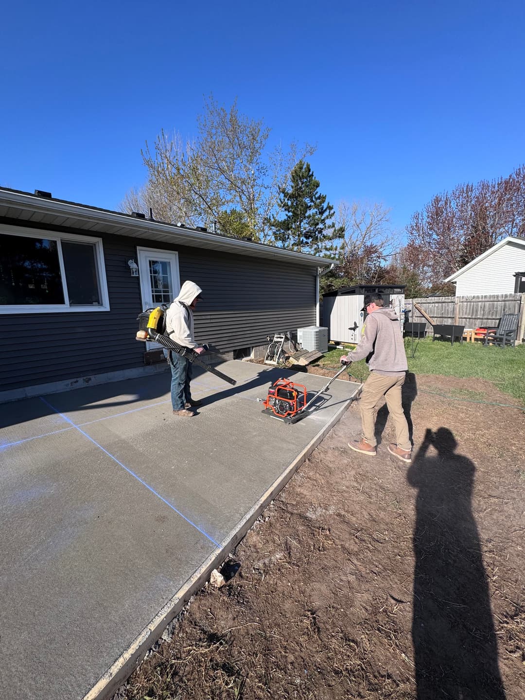 Two workers leveling freshly poured concrete on a residential patio with tools and equipment.
