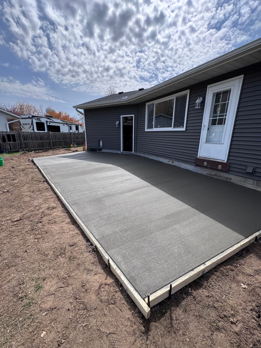 Freshly poured concrete patio beside a house under a cloudy sky, ready for use.