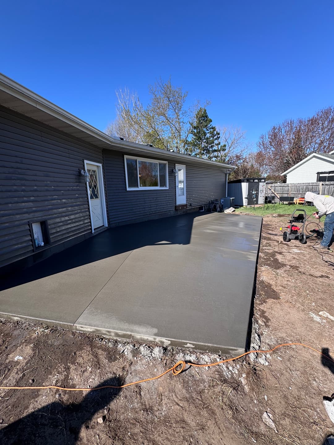 Freshly poured concrete patio in a residential backyard with workers preparing the area.